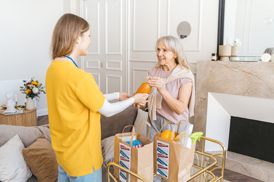 A helper delivering groceries to a happy senior woman at home